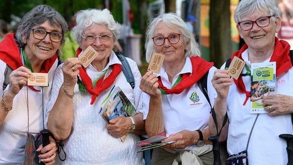 Die Wanderfreundinnen Helga (l-r), Marianne, Karin und Anni halten auf der Festmeile beim 122. Deutschen Wandertag 2024 ein Holzschild «Sagenhaft. Grenzenlos.», dem Motto der Veranstaltung.