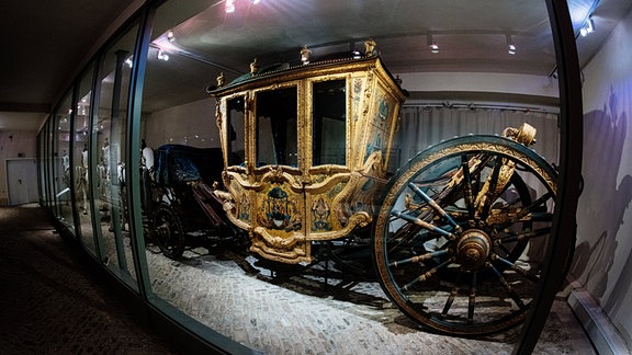 Eine prunkvolle goldene Kutsche steht im Schlossmuseum Sondershausen hinter einer Glasscheibe.