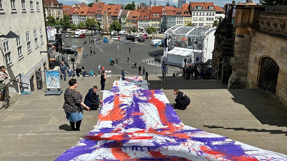 Blick vom oberen Ende der Domstufen Richtung Domplatz. Mittig ist ein riesiges Banner ausgerollt. Es ist bunt gemustert.