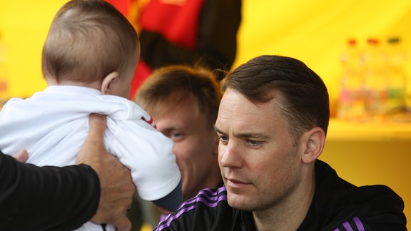 Ein Baby wird vor manuel Neuer gehalten. 