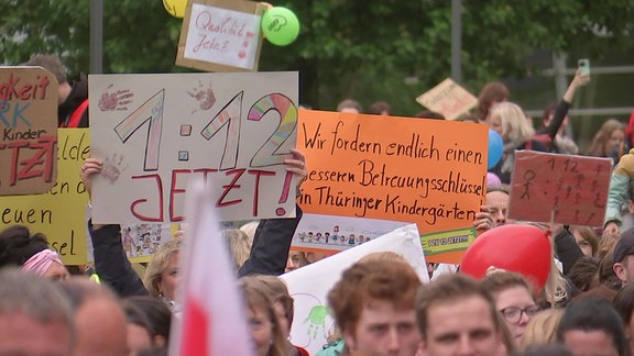 Mehrere Menschen halten Plakate in die Luft mit Forderungen für einen besseren Betreuungsschlüssel.