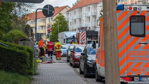 Feuerwehrleute stehen auf einem Gehweg neben parkenden Autos.