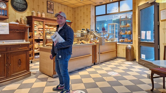 Mann mit Zeitung unter dem Arm in einer Bäckerei