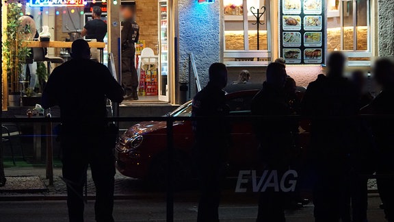  Polizisten stehen im Dunkeln vor einem Imbiss in Erfurt.