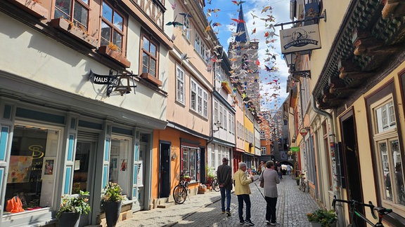 Mehrere Menschen laufen über die Krämerbrücke, die mit Kranichen aus Papier geschmückt ist.