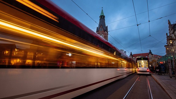 Eine Straßenbahn fährt abends über den Erfurter Anger, die zweite steht an der Haltestelle.