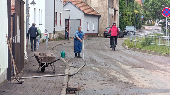 Menschen räumen nach Überflutung Schlamm von einer Straße.