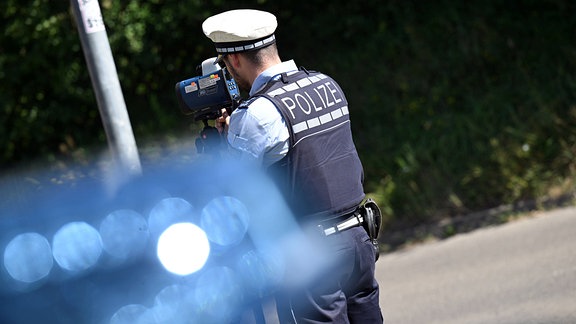 Ein Polizist überwacht mit einem Laserhandmessgerät, auch Laserpistole oder Radarpistole genannt, die Geschwindigkeit im Straßenverkehr.