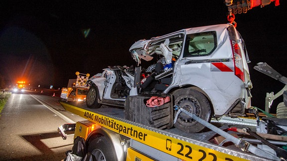 Ein total zerstörter Unfallwagen auf einem Abschlepper in der Nacht.