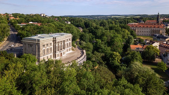 Blick von oben auf ein großes historisches Gebäude, umgeben von Bäumen 