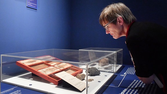 Eine Frau beugt sich über eine Ausstellungsvitrine.