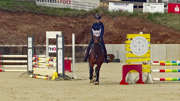 Ein Mädchen reitet auf einem Pferd über den Reitplatz