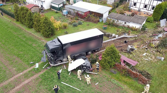 Ein Lkw steht nach einem Unfall auf einem Feld. In einem Graten hinter ihm ist eine Schneise der Verwüstung. Neben dem Lkw steht ein Auto. Es ist nach einem Zusammenprall zerstört. Auf dem Dach des Autos liegt ein Wellblech.