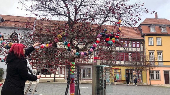 Ein Frau schmückt einen Baum mit Wollschmuck.