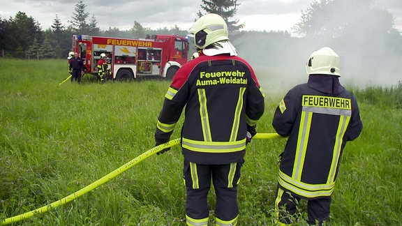 Feuerwehrleute mit Auto auf einer Wiese mit Rauche