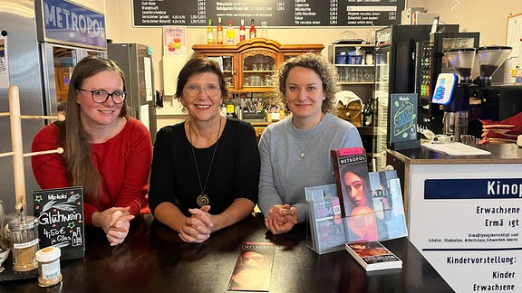 Drei lächelnde Frauen stehen nebeneinander hinter dem Verkaufstresen im Metropol Kino Gera. 