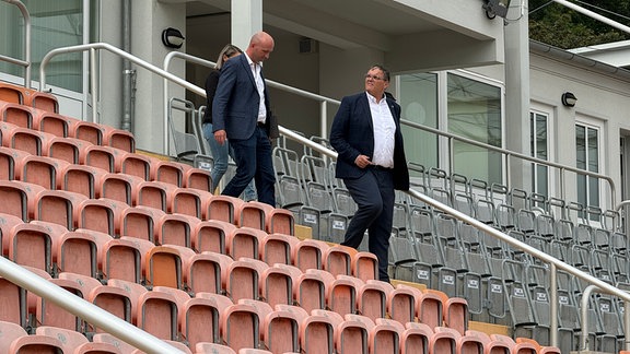 3 Personen vor der Tribühne eines Stadions