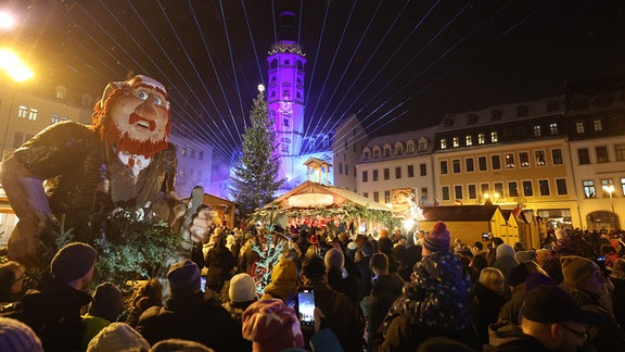 Besucher stehen bei der Eröffnung des Weihnachtsmarktes, auf dem Märchenmarkt und betrachten eine Lasershow mit der Darstellung des Märchens âDas tapfere Schneiderleinâ am Rathausturm.