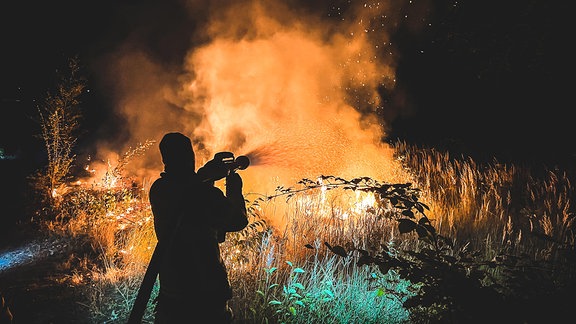 Ein Feuerwehrmann löscht bei Nacht einen Waldbrand