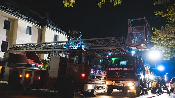 Feuerwehrautos mit Blaulicht und Drehleiter bei einem Einsatz in einer nächtlichen Straße 