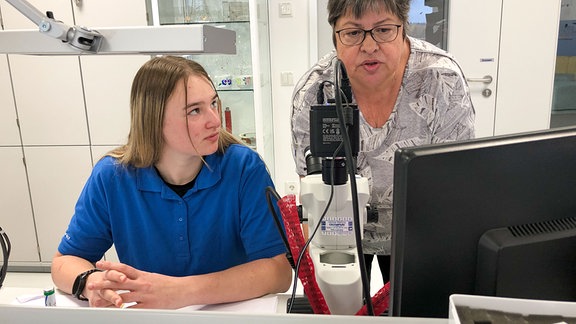 Eine Frau erklärt einer Auszubildenden etwas am Computer.