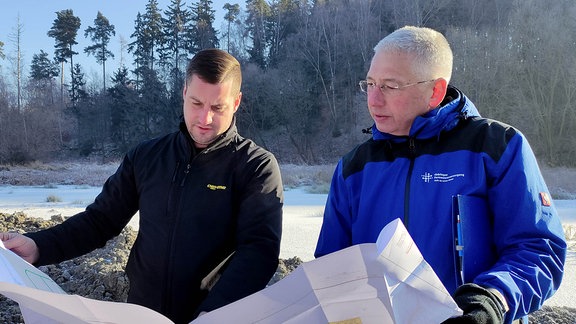 Zwei Männer lesen einen Plan auf einer Baustelle