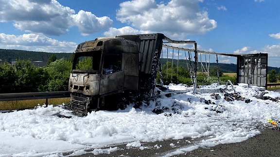 Ein ausgebrannter Lkw auf einer Autobahn mit sehr viel Löschschaum