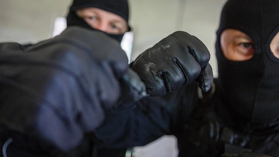 Zwei aggressive Männer mit Sturmhauben und Handschuhen.