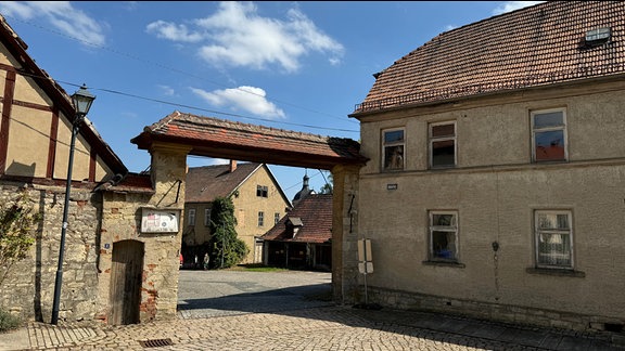 Blick auf einen gepflasterten Hof und einen Torbogen. 