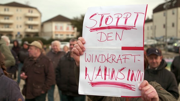 Ein Mensch hält ein Plakat mit der Aufschrift "Stoppt den Windkraft-Wahnsinn".