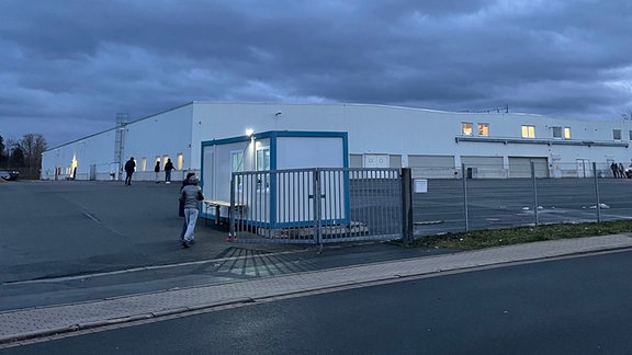 Menschen laufen auf eine große Lagerhalle zu.