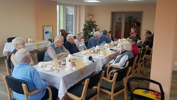 Mehrere Menschen sitzen zusammen an einer langen Tafel und trinken Kaffee.