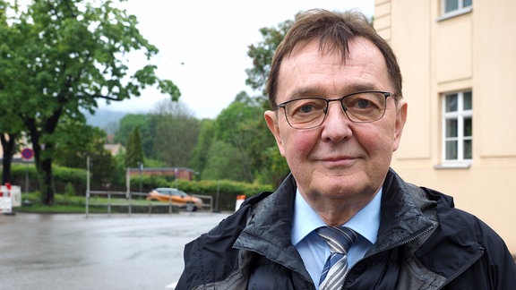 Karlheinz Frosch vor dem Landtratsamt im Kreis Saalfeld-Rudolstadt. Er trägt Brille, Schlips und eine wattierte Jacke.