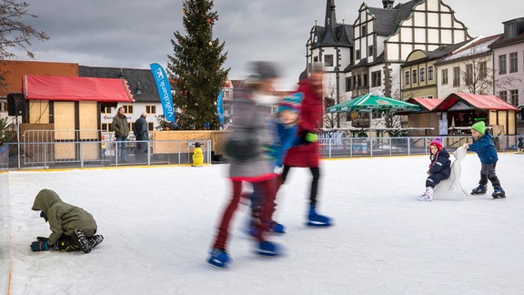 Kinder laufen mit Schlittschuhen über die Eisbahn.