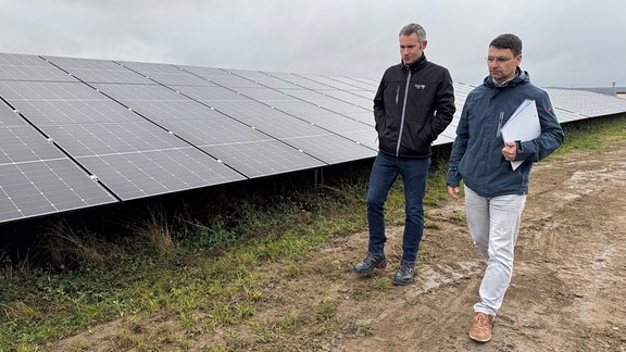 Zwei Männer laufen an einem Solarfeld vorbei.