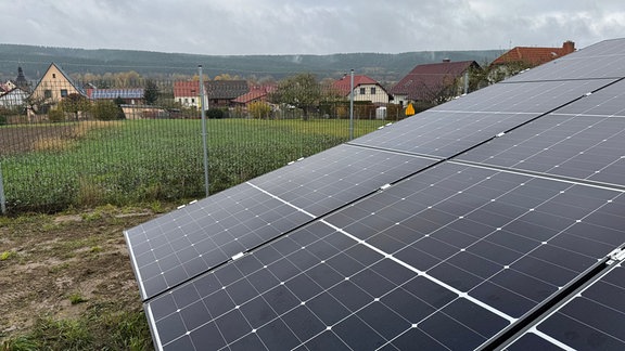 Solaranlagenfeld auf einer Wiese, im Hintergrund ein Dorf 