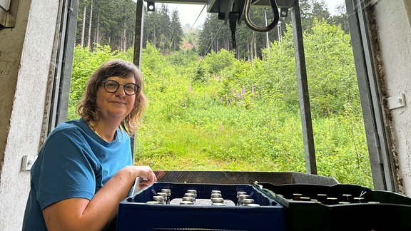 Eine Frau neben einer mit Getränkekästen beladenen Gondel einer Materialseilbahn