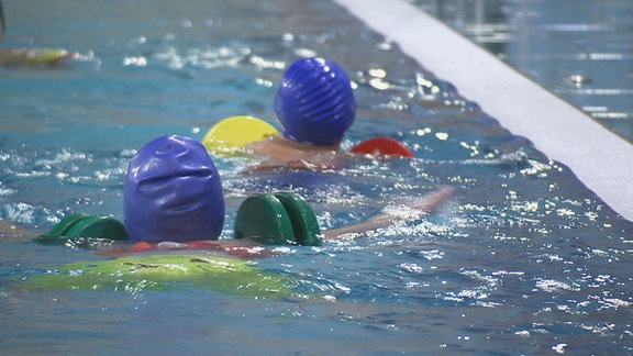 Kinder schwimmen mit Schwimmhilfen in einem Hallenbad