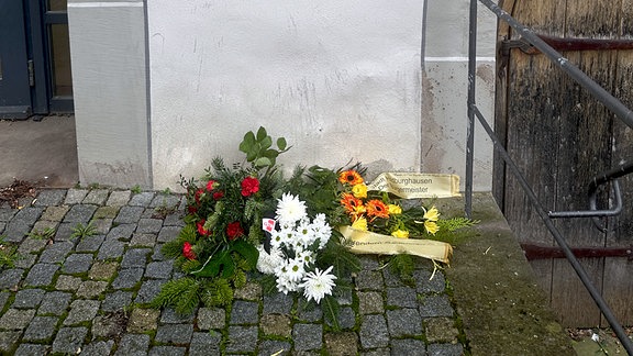 Ein Blumenkranz liegt unter einer Gedenktafel an, auf der steht "An diesem Ort wurde über das Schicksal unserer letzten jüdischen Mitbürger entschieden. Den Opfern zum Gedenken. Den Lebenden zur Mahnung." 