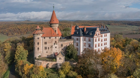 Eine historische Burg erhebt sich in einer herbstlichen Landschaft.