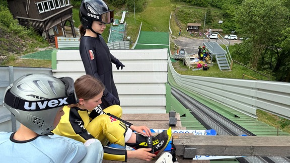 Drei Kinder bereiten sich auf das Springen von einer Skisprungschanze vor.