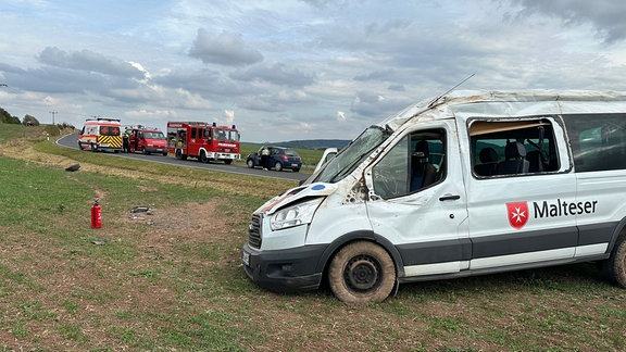 Ein Transporter steht nach einem Unfall in einem Feld, im Hintergrund mehrere Rettungsfahrzeuge.