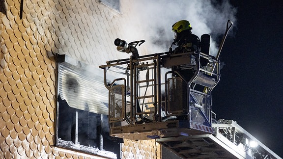 Ein Feuerwehrmann an einem rauchenden Fenster.