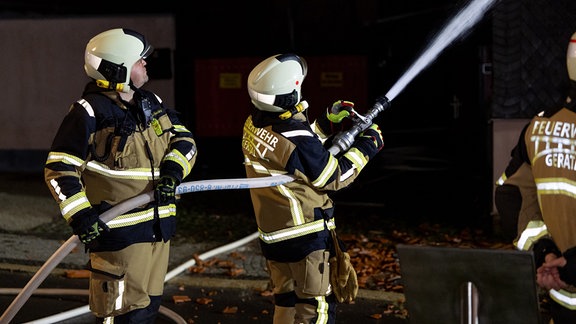 Zwei Feuerwehrleute löschen mit einem Schlauch.