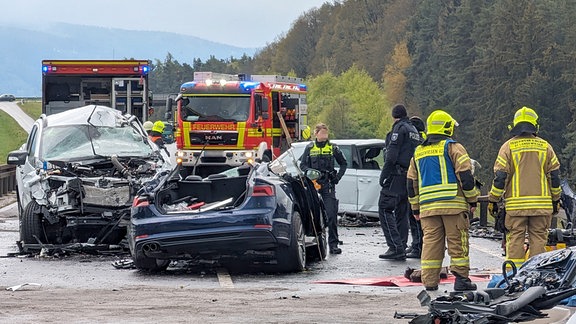 Nach einem schweren Unfall stehen drei stark beschädigte Autos sowie Fahrzeuge der Feuerwehr und Polizisten und Feuerwehrleute auf der B88.