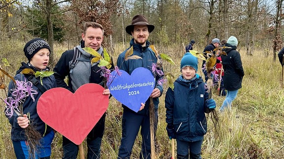 Männer und Jungen mit gebastelten Herzen bei einer Baumpflanzaktion im Wald