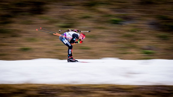 Ein Biathlon-Athlet auf der Strecke, in einer schneefreien Umgebung.