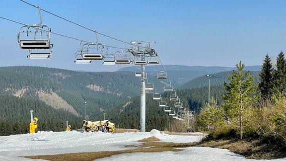 Teilweise geschmolzene Schneedecke unter einem Skilift in Oberhof. Unter dem Lift stehen Schneekanonen.