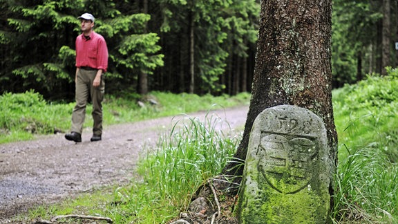 Historischer Grenzstein an der Grenze von Fürstentümern, hinten ein Wanderer.