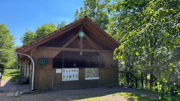 Eine Wanderhütte aus Holz steht neben ein paar Bäumen.